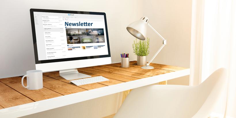 A computer stands on a desk. A newsletter can be seen on the computer screen.